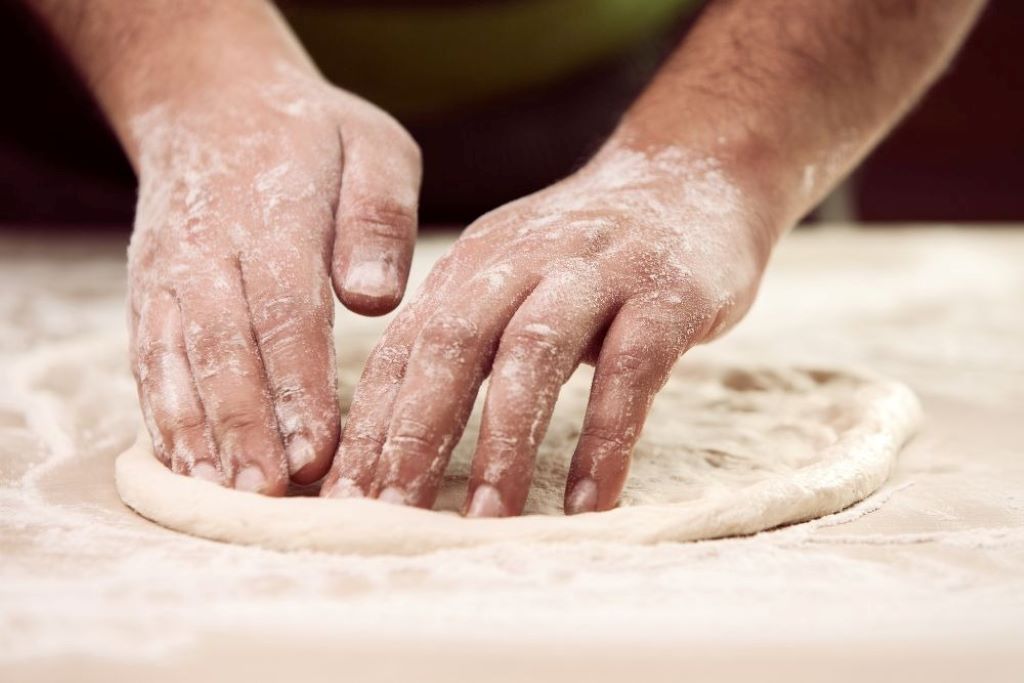 Hands preparing homemade pizza dough from scratch using an Ooni pizza oven, highlighting texture and elasticity