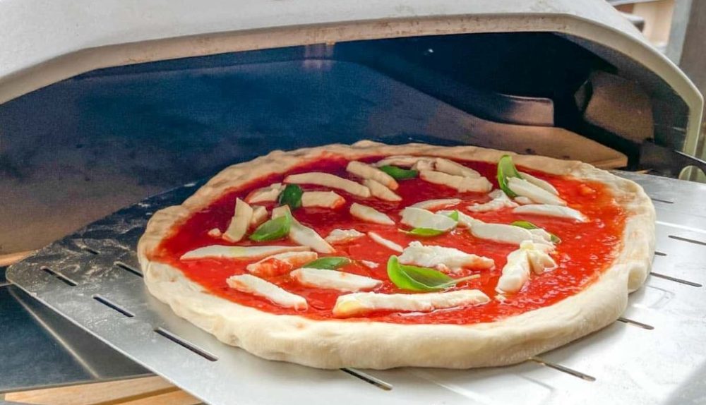 Close-up of a perfectly stretched Ooni pizza dough topped with fresh ingredients, ready to bake in a home oven