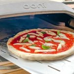 Close-up of a perfectly stretched Ooni pizza dough topped with fresh ingredients, ready to bake in a home oven