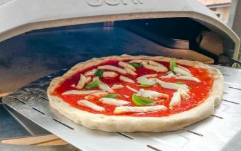 Close-up of a perfectly stretched Ooni pizza dough topped with fresh ingredients, ready to bake in a home oven