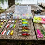 A colorful beginner fishing lure kit spread on a wooden surface showing spinners, spoons, crankbaits, and soft plastic baits in various sizes
