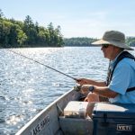 An angler wearing a wide-brim UPF 50+ fishing hat on a sunny lake, with water reflecting sunlight