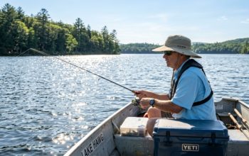 An angler wearing a wide-brim UPF 50+ fishing hat on a sunny lake, with water reflecting sunlight