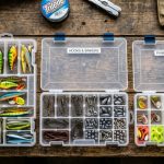 Open tackle backpack with stacked organized utility trays on boat deck.