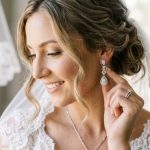 Bride touching sparkling diamond-drop earrings on her wedding day.